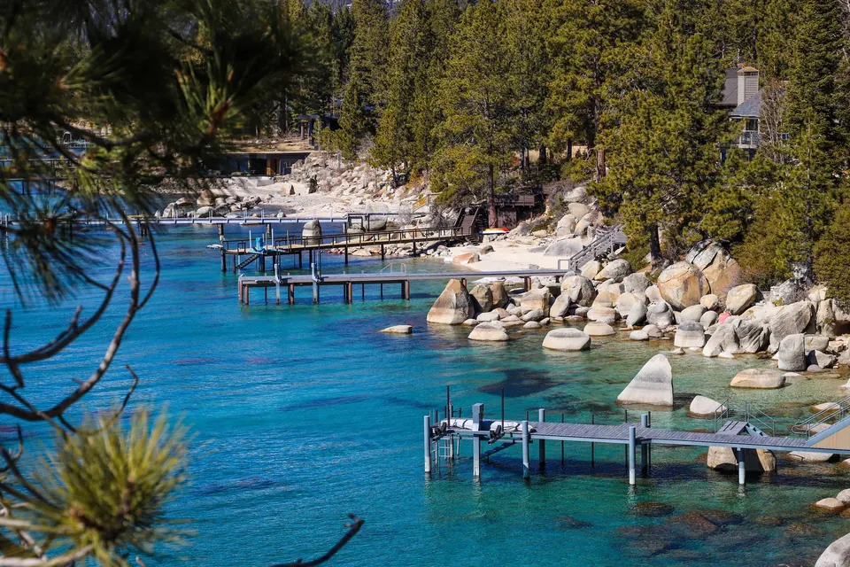 Private piers reaching over clear turquoise water along a granite-boulder shoreline on Lake Tahoe